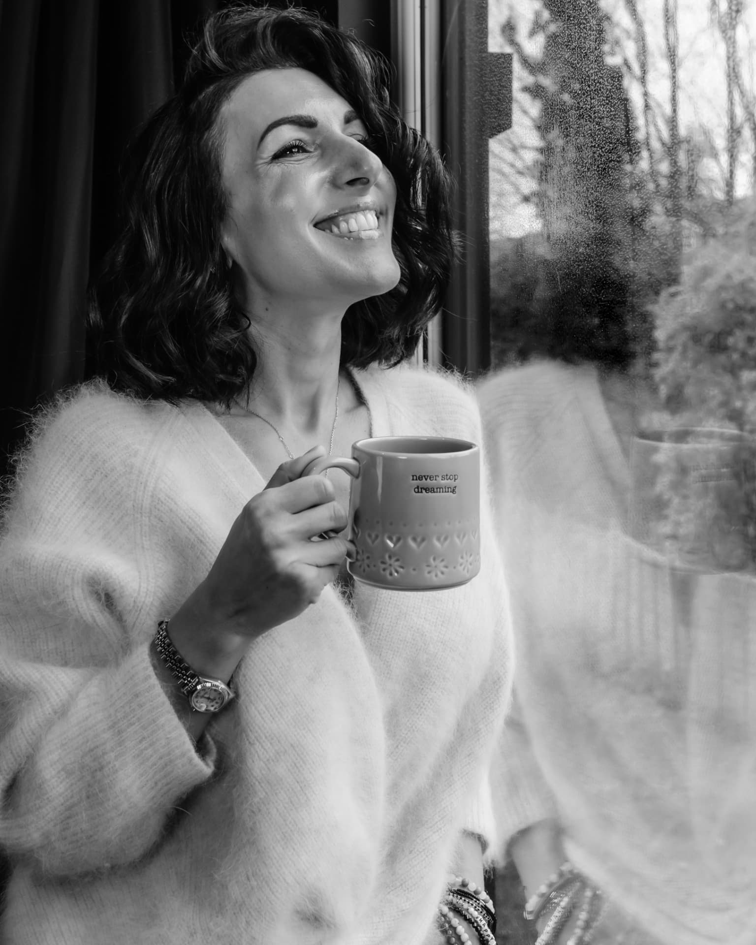 Black and white portrait of Naomi Buff holding a mug by a window