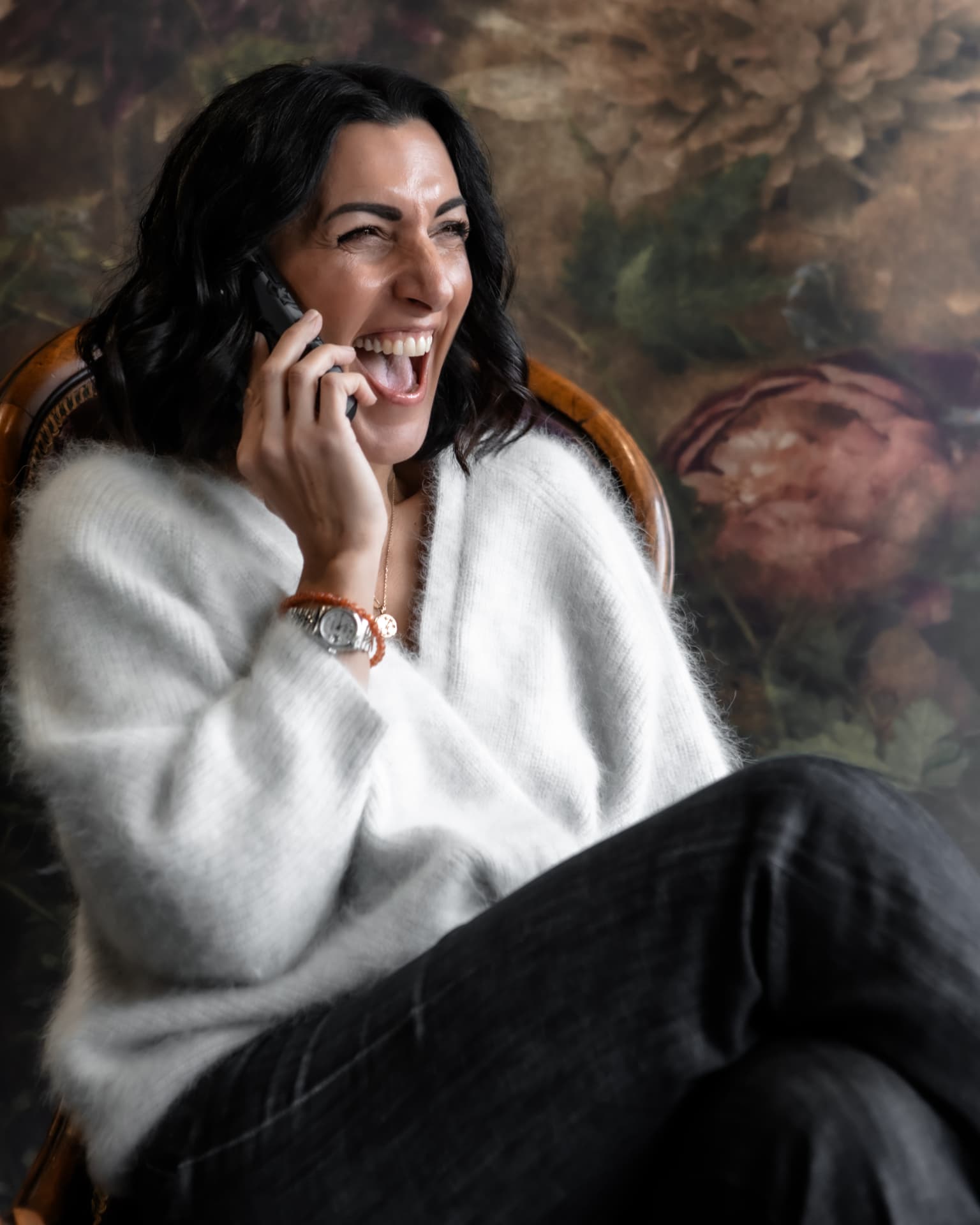 Naomi Buff laughing during a phone call in a cream knit cardigan