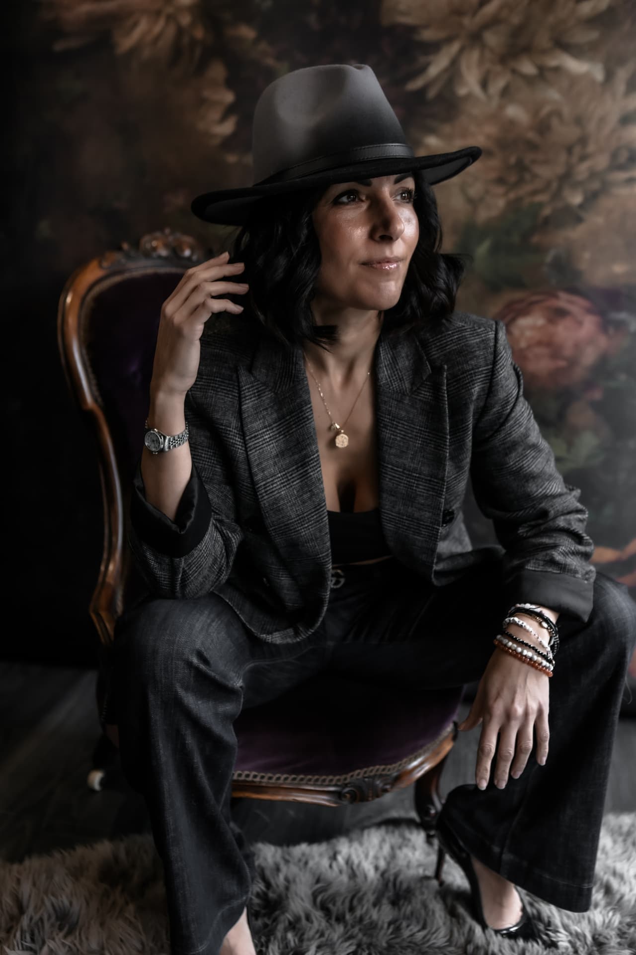 Naomi Buff seated in a velvet chair wearing a tailored suit and hat